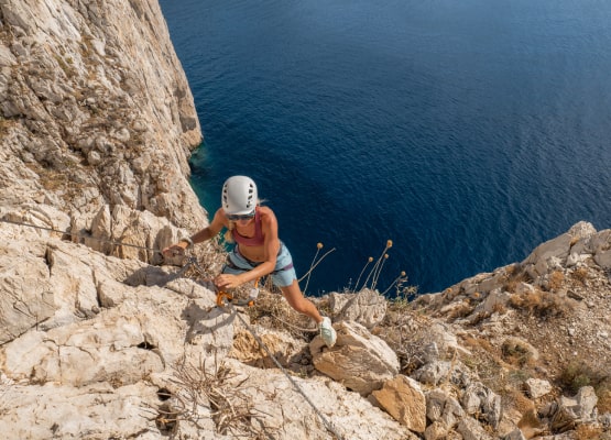 une femme qui escalade une paroie rocheuse au dessus de la mer