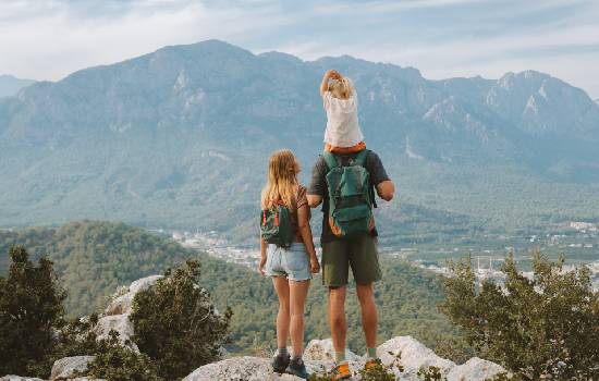 Une famille avec un enfant sur les épaules de son papa regardant un paysage de montagne. 